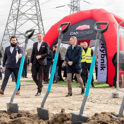 Nowoczesne centrum materiałowe w Rybniku, symboliczna łopata w ziemi, inwestycja CADesigner Engineering. (wygenerowano przez AI)