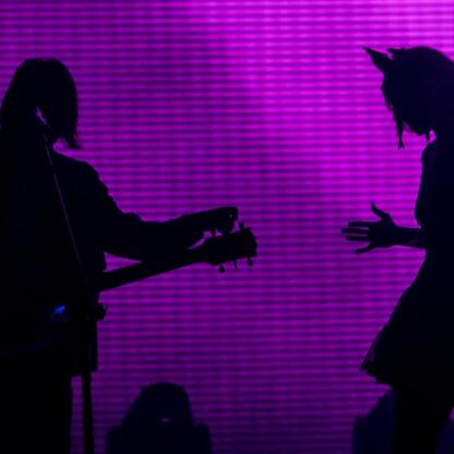 Silhouette of performers on stage, one playing keyboard, the other dancing, against a vibrant purple backdrop. (wygenerowano przez AI)