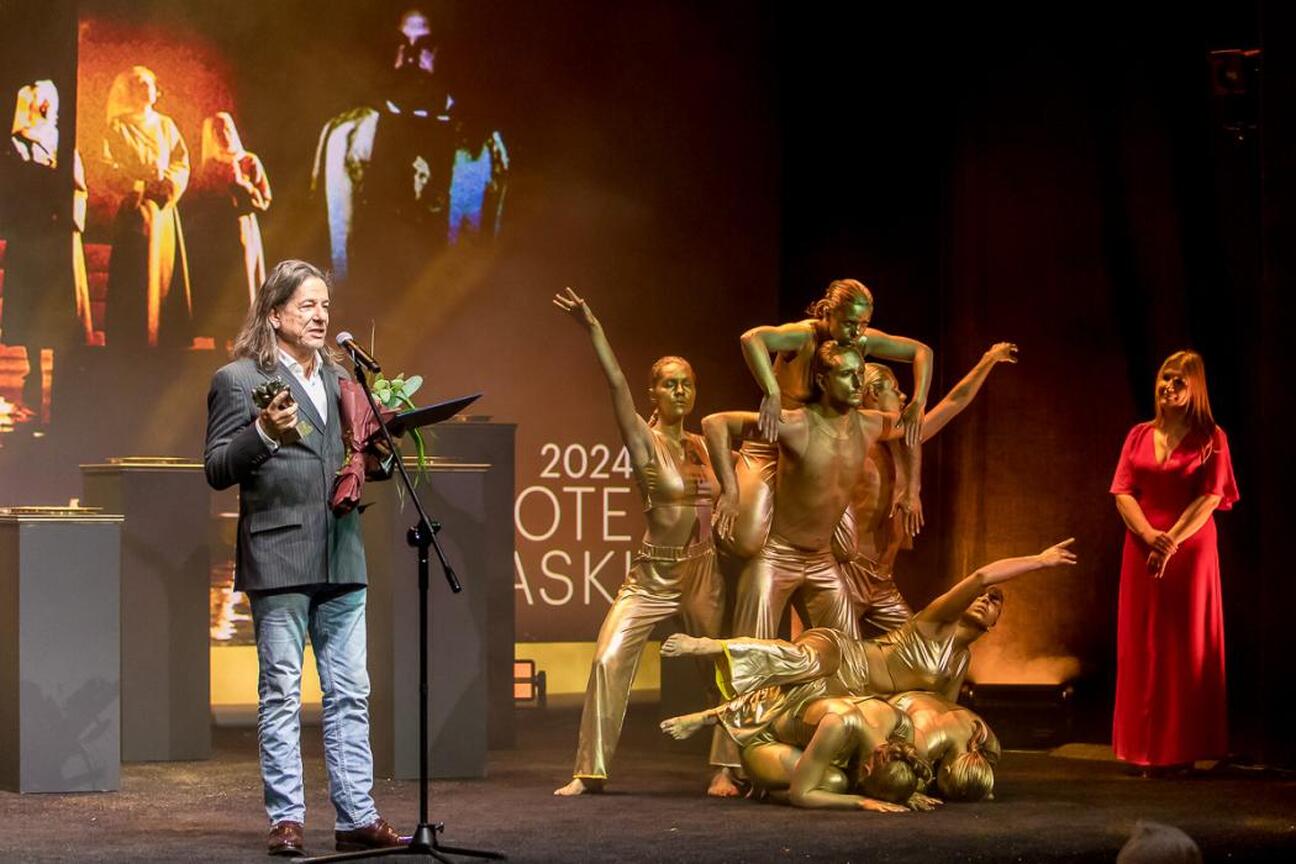 Widoczna jest scena z spektaklu "Diabły" Mai Kleczewskiej, nagrodzonego Złotą Maską za najlepszy spektakl roku. Scena oświetlona jest purpurowym światłem, z aktywnymi aktorami na scenie. (wygenerowano przez AI)
