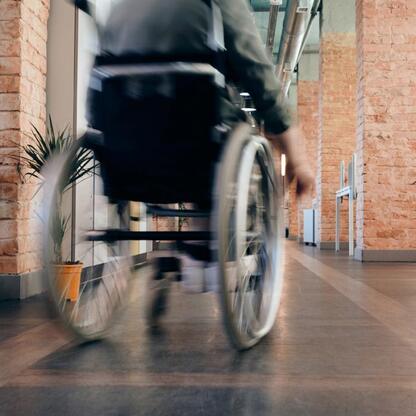 Osoba w wózku inwalidzkim porusza się po nowoczesnym biurze z ceglanymi ścianami i szafami w stylu przemysłowym, podkreślając temat dostępności i inkluzji. (wygenerowano przez AI)