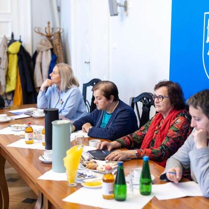 Grupa ludzi w rozmowie w sali konferencyjnej, przygotowująca uroczystości 50-lecia Uniwersytetu Trzeciego Wieku. (wygenerowano przez AI)