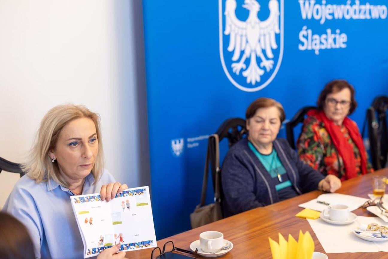 Grupa ludzi w rozmowie w konferencyjnym pomieszczeniu z logo Województwa Śląskiego. (wygenerowano przez AI)