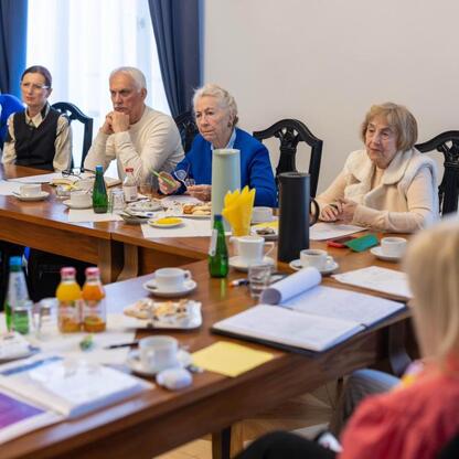 Grupa dorosłych uczestniczy w spotkaniu organizacyjnym w Gmachu Sejmu Śląskiego, przygotowując uroczystości z okazji 50-lecia Uniwersytetu Trzeciego Wieku. (wygenerowano przez AI)