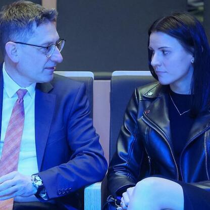 Dwóch uczestników konferencji energetycznej w Tychach, w czarnych garniturach i kurtce, omawiają wyzwania transformacji energetycznej. (wygenerowano przez AI)