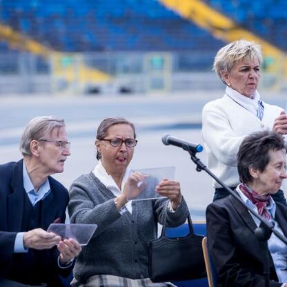 Grupa ludzi w sztandarowym uroczystym ustawieniu na stadionie, uczestniczący w dyskusji o aktywizacji młodzieży. (wygenerowano przez AI)