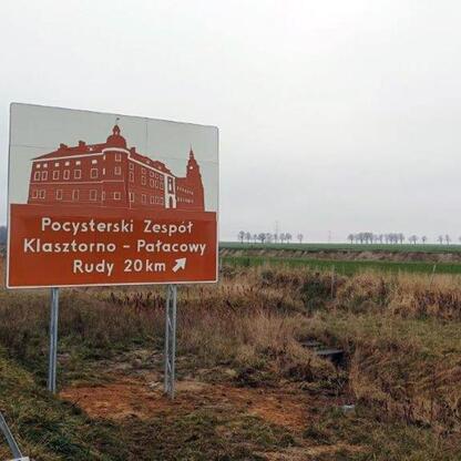 Znak drogowy w regionie Górnej Odry wskazuje na Pocysterski Zespół Klasztorno-Pałacowy w Rudach, 20 km dalej. (wygenerowano przez AI)