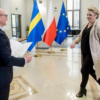 Wicemarszałek Województwa Śląskiego Grzegorz Boski prezentuje dokument w trakcie formalnego spotkania w modernistycznym biurze, gdzie widoczne są flagi Polski, Szwecji i Unii Europejskiej. (wygenerowano przez AI)