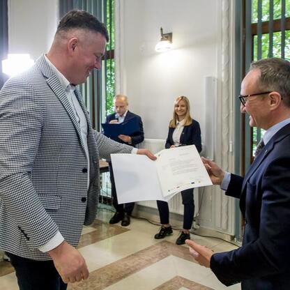 Wicemarszałek Województwa Śląskiego, Grzegorz Boski, wręcza beneficjentom Europejskiej Unii Fundusze dla projektów poprawy efektywności energetycznej, ochrony przyrody, budowy tras rowerowych i rekult (wygenerowano przez AI)
