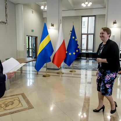 Wicemarszałek Województwa Śląskiego Grzegorz Boski wręcza dokument kobiecie w kwietnikowej sukience podczas ceremonii związanych z funduszami europejskimi dla regionu. (wygenerowano przez AI)