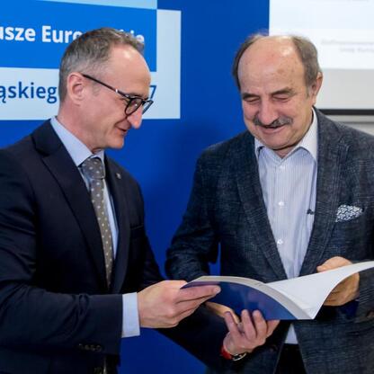 Grzegorz Boski, wicemarszałek Województwa Śląskiego, wręcza dokument Marcinowi Ryśowi, koordynatorowi projektów z Funduszy Europejskich dla Śląska 2021-2027. (wygenerowano przez AI)