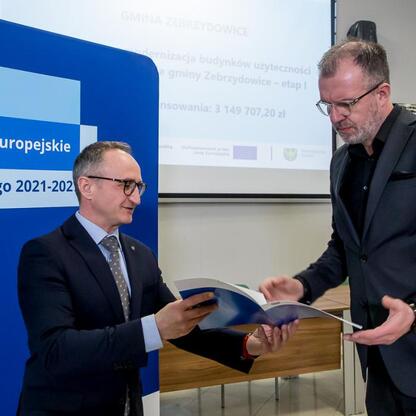 Grzegorz Boski, wicemarszałek Województwa Śląskiego, wręcza dokumenty przed logo Funduszy Europejskich dla Śląska 2021-2027. (wygenerowano przez AI)