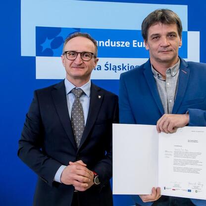 Grzegorz Boski, wicemarszałek Województwa Śląskiego, wręcza dokumenty podczas uroczystości związanego z alokacją funduszy europejskich dla regionu Śląskiego. (wygenerowano przez AI)
