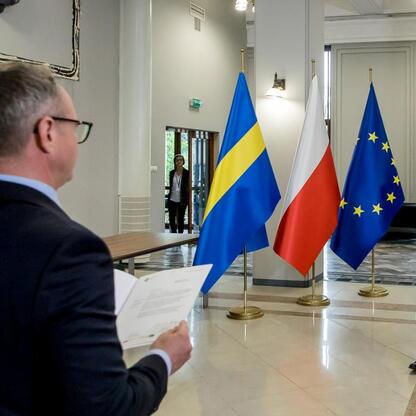 Widoczne są dwaj mężczyźni w garniturach, którzy prawdopodobnie uczestniczą w ceremonii podpisania dokumentów, związanych z fundowaniem regionalnych projektów województwa śląskiego. (wygenerowano przez AI)