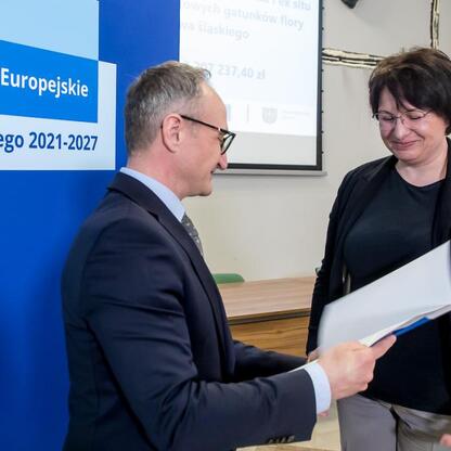 Wicemarszałek Grzegorz Boski wręcza dokument kobiecie w ramach ceremonii Funduszy Europejskich dla Śląska 2021-2027. (wygenerowano przez AI)