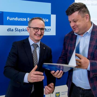 Grzegorz Boski, wicemarszałek Województwa Śląskiego, wręcza dokumenty przed logo Funduszy Europejskich dla Śląska 2027. (wygenerowano przez AI)