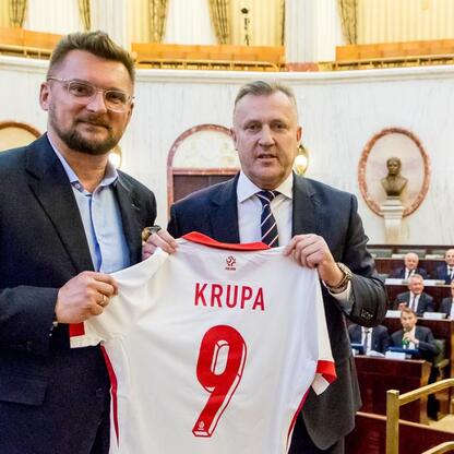 Dwóch mężczyzn w strojach formalnych, trzymających koszulkę z imieniem 
