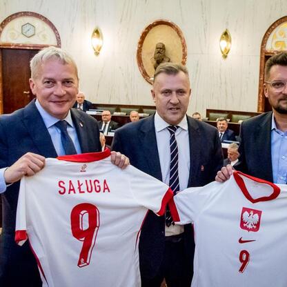 Trzech mężczyzn w strojach formalnych trzymają koszulki z numerem 9 i nazwą 
