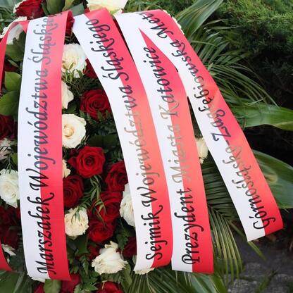 Floralna kompozycja z czerwonymi i białymi wstążkami, upamiętniająca 104. rocznicę III Powstania Śląskiego w Katowicach. (wygenerowano przez AI)