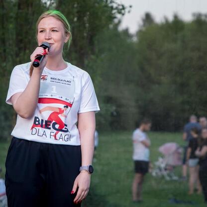 Joanna Bojczuk, członkini Zarządu Województwa Śląskiego, prowadzi mikrofonem na Biegu dla Flagi 2025 w Parku Śląskim. (wygenerowano przez AI)