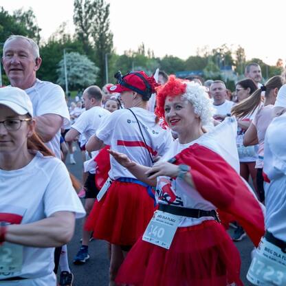Bieg dla Flagi 2025 w Parku Śląskim, uczestnicy w białych koszulkach z czerwono-białymi pasami, jedna w czerwonym tutu i perukie. (wygenerowano przez AI)