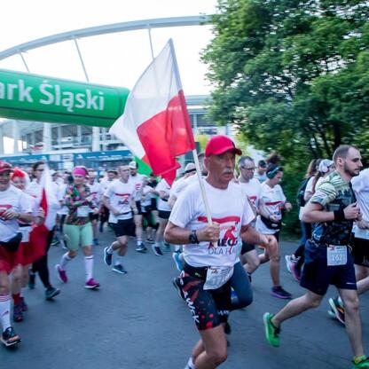 Bieg dla Flagi 2025 w Parku Śląskim, uczestnicy w białych koszulkach z czerwonymi akcentami, jedni biegną, inni machają flagą Polski. Atmosfera patriotyczna i energetyczna. (wygenerowano przez AI)