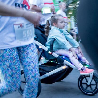 Na Biegu dla Flagi 2025 w Parku Śląskim: dziewczynka w niebieskim dżetku i spódce spacerowana przez uczestnika z numerem 551. (wygenerowano przez AI)