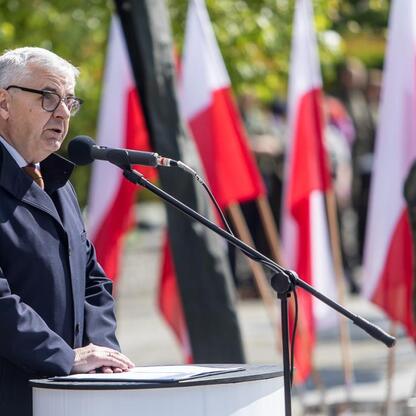 Formalna uroczystość w Katowicach, upamiętniająca 80. rocznicę zakończenia II wojny światowej w Europie. Mężczyzna w garniturze przemawia z podium, za nim żołnierz w mundurze. (wygenerowano przez AI)