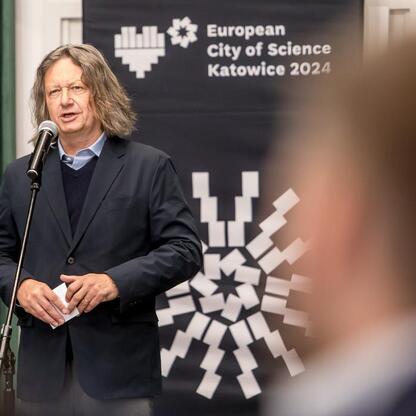 Mężczyzna w czarnej kamizelce przemawia na podium podczas Forum Przyszłości Miasta Nauki w Katowicach. (wygenerowano przez AI)