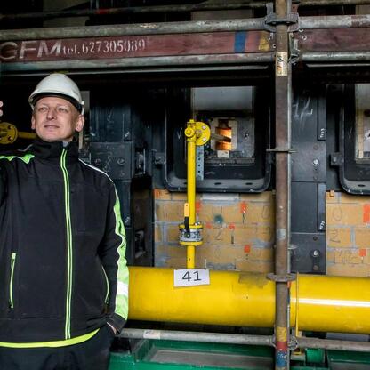 Pracownik JSW Koks w hard hat i kamizelce ochronnej robi selfie przed nowoczesną baterią koksowniczą w Dąbrowie Górniczej. (wygenerowano przez AI)
