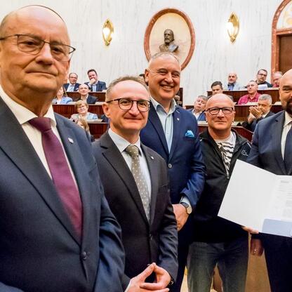 Wicemarszałek Grzegorz Boski wręcza certyfikaty 40 przedstawicielom Rodzinnych Ogrodów Działkowych w Sali Sejmu Śląskiego. (wygenerowano przez AI)