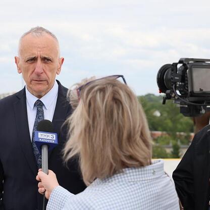 Wicemarszałek Leszek Pietraszek w rozmowie z dziennikarzem TVP3 Katowice podczas otwarcia nowego helipadu dla helikopterów ratunkowych w Centrum Zdrowia Dziecka i Rodziny im. Jana Pawła II w Sosnowcu. (wygenerowano przez AI)