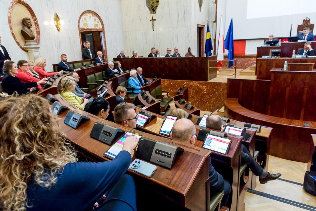 Dwa parlamentarzyści w rozmowie w sali posiedzeń Sejmiku Śląskiego, omawiają Krajowy Plan Odbudowy i budżet 2025. (wygenerowano przez AI)