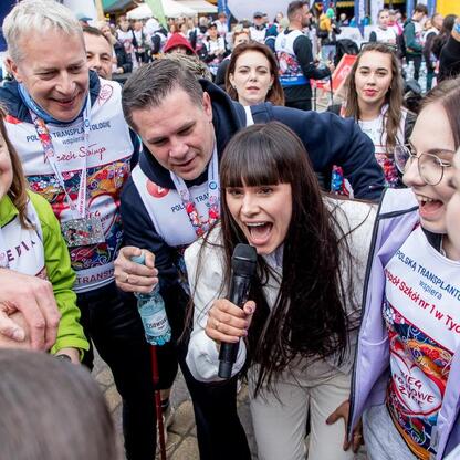 Zwycięski moment 26. Bieg po Nowe Życie, wspierający polską transplantologię przez 14 lat. Marszałek Wojciech Saługa i uczestnicy w niebieskich kurtkach z żółtym logo. (wygenerowano przez AI)