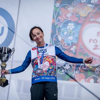 Zdjęcie przedstawia uczestnika 26. Bieg po Nowe Życie, trzymającego trofeum, na tle muralu z napisem 