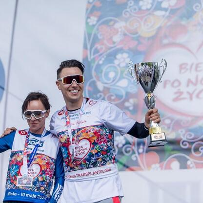 Zdjęcie przedstawia trzech zwycięzców 26. Biegu po Nowe Życie, trzymających trofea i medal, ubranych w koszulki z logo i hasłem 