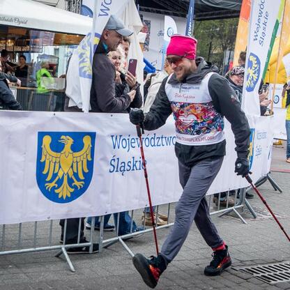 Bieg po Nowe Życie, 26 edycja, Piotr Kupicha, uśmiechnięty, czerwony szal, żółto-niebieska kamizelka, marsz z okrzykami, Silesia. (wygenerowano przez AI)