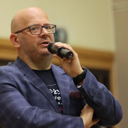 Mężczyzna w niebieskim płaszczu przemawia do mikrofonu na festiwalu literackim Festiwal Słowa im. Jerzego Pilcha 