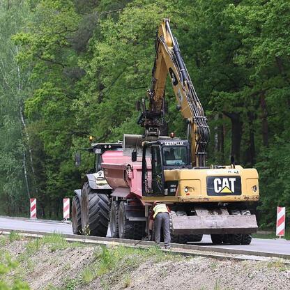 Na budowie drogi wojewódzkiej DW 928, modernizacji prowadzonej przez Budimex S.A., widoczny jest Ciągnik Caterpillar, a pracownicy kontrolują jego stan. (wygenerowano przez AI)