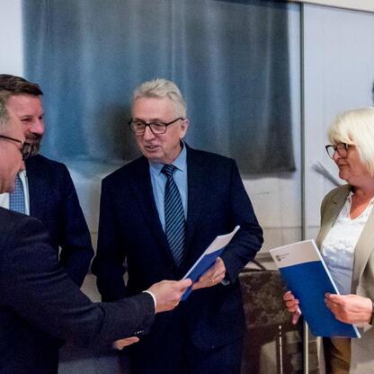 Grupa czterech osób w strojach formalnych, dyskutujących w sali konferencyjnej, podczas ceremonii wręczenia umów w ramach Inicjatywy Sołeckiej w Subregionie Południowym. (wygenerowano przez AI)