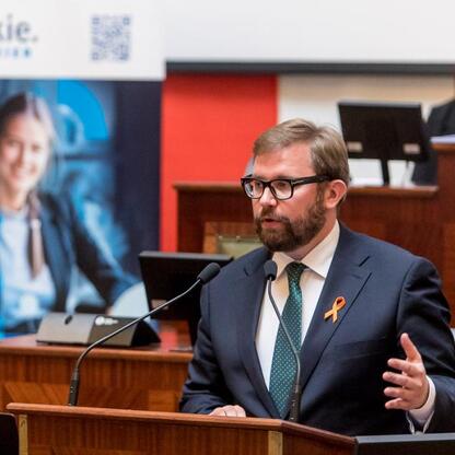 Mężczyzna przemawia na podium podczas konferencji o wielu aspektach stwardnienia rozsianego w Sali Sejmu Śląskiego. (wygenerowano przez AI)