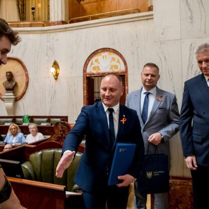 Na zdjęciu: Rafał Adamczyk, członek Zarządu Województwa Śląskiego, szczerzy uśmiech, podczas konferencji o stwardnieniu rozsianym w Sali Sejmu Śląskiego. (wygenerowano przez AI)