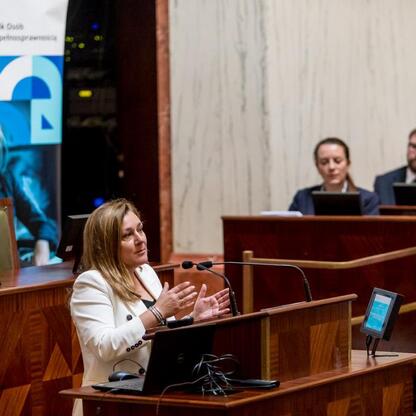 Konferencja o stwardnieniu rozsianym w Sali Sejmikowej, gdzie kobieta w białym płaszczu przemawia do publiczności. (wygenerowano przez AI)