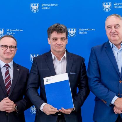 Trzech mężczyzn przed emblematem Województwa Śląskiego, prezentują umowy modernizacji dróg wiejskich. (wygenerowano przez AI)