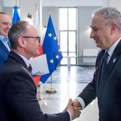 Trzech mężczyzn w strojach urzędniczych trzyma się za ręce w oficjalnym kontekście, związany z modernizacją dróg dojazdowych do terenów wiejskich województwa śląskiego. (wygenerowano przez AI)