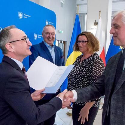 Wicemarszałek Grzegorz Boski i Marek Bieniek podczas ceremonii wręczenia umów na modernizację dróg dojazdowych do terenów wiejskich. (wygenerowano przez AI)