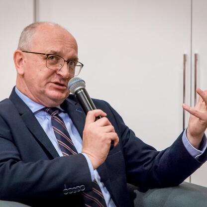 Mężczyzna w garniturze przemawia do publiczności, gestykulując, podczas uroczystości jubileuszowej Muzeum „Górnośląski Park Etnograficzny w Chorzowie”. (wygenerowano przez AI)