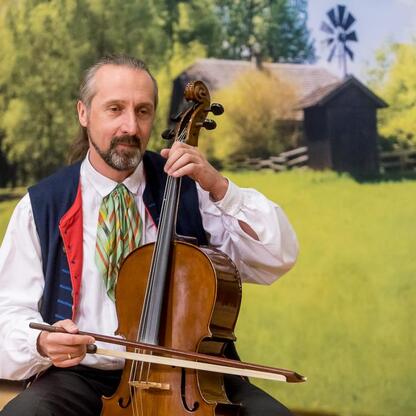 Muzyk gra na cello w tradycyjnym, rolniczym krajobrazie, z wiatrakiem i drewnianym domem na tle. (wygenerowano przez AI)