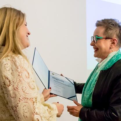 Podczas Święta Muzealnictwa w Muzeum Historii Katowic, dwie damy wręczają Nagrody Marszałka Województwa Śląskiego za Wydarzenie Muzealne roku 2024. (wygenerowano przez AI)