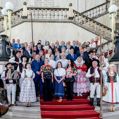 Zbliżenie na grupę ludzi w tradycyjnych strojach folkowych na schodach Sejmiku Województwa Śląskiego, uczestnicy Tygodnia Kultury Beskidzkiej. (wygenerowano przez AI)
