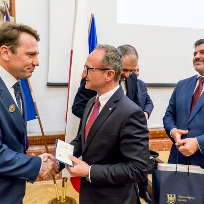 Wicemarszałek Województwa Śląskiego Grzegorz Boski uczestniczy w formalnym spotkaniu w Sejmiku Województwa Śląskiego, gdzie oficjalnie podpisuje dokumenty i wymienia się rękawiczkami. (wygenerowano przez AI)